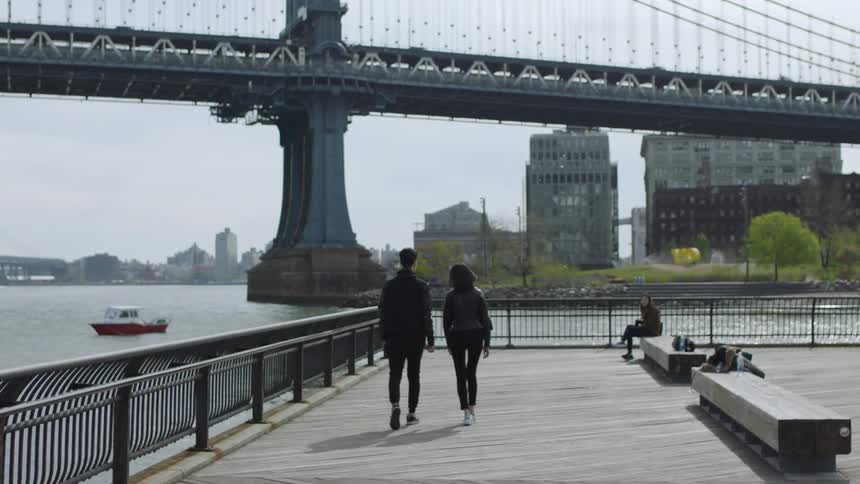 A man and woman walk on a city pier on the harbor
