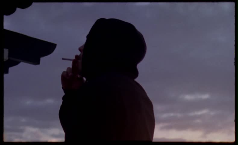 A man in a hoodie is smoking at dusk