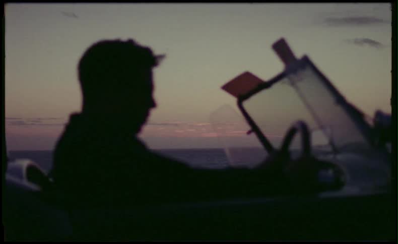 A man driving a convertible car near the ocean at sunset