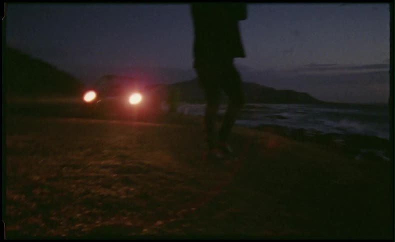 Man standing in front of car headlights walking toward the beach