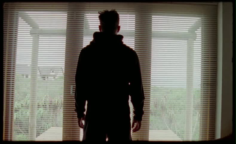 Window blinds open and close and a man stands in front of them