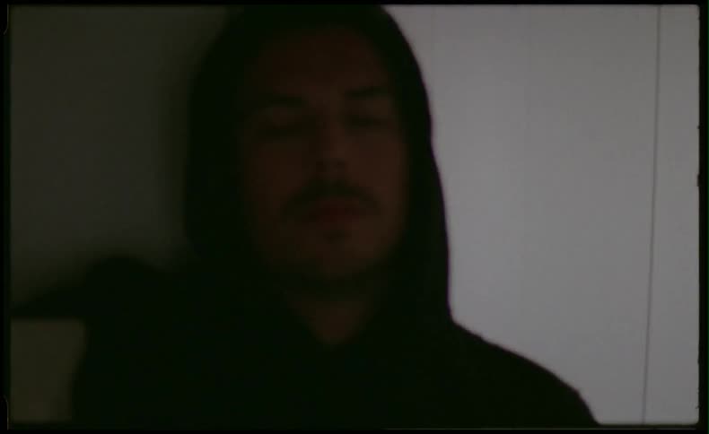 Man wearing a hood is turning a light on and off in a room