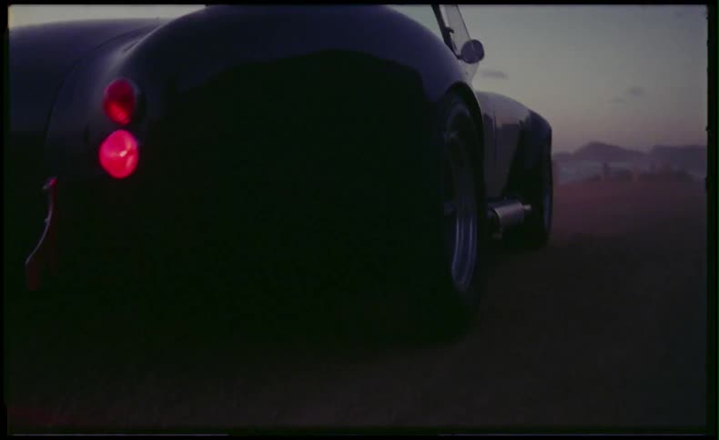Man driving up to a beach in a classic sports car at dusk