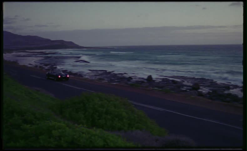 Classic sports car driving down coastal road at sunset