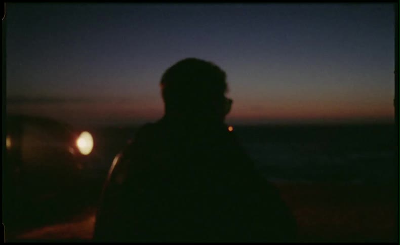 Man standing in front of car headlights looking at the sunset