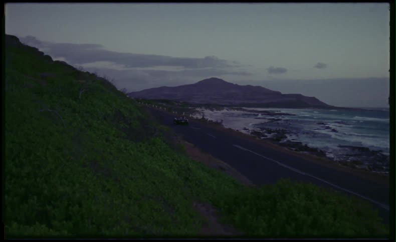 Classic sports car driving down coastal road at sunset