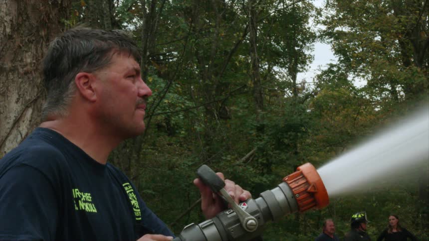Fireman holding a hose with a strong stream of water coming out of it in a wooded area