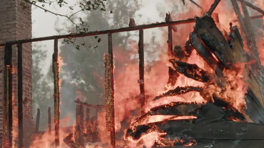 A brick chimney remains as a house burns