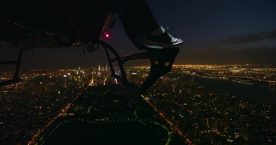 A man reaches his legs out of a flying helicopter