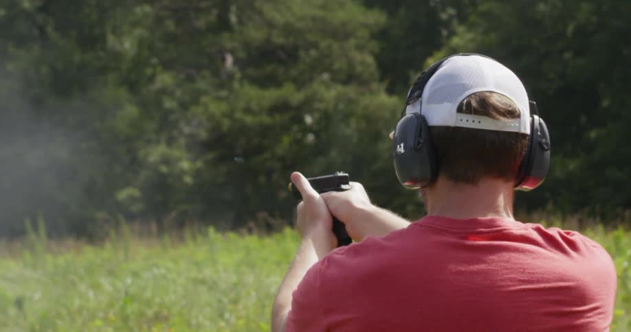 Man shooting a handgun in a wooded area while wearing ear protection