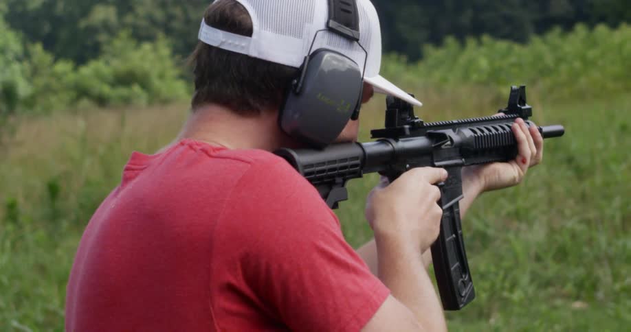 Man shooting a rifle in a wooded area while wearing ear protection