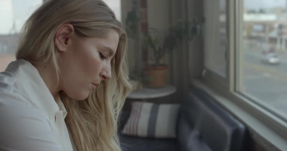Woman stands near a window in an apartment as cars drive outside