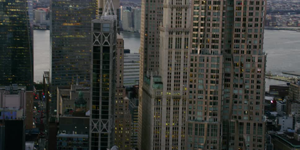 Smoke pours from stacks on the rooftops of buildings in a city at dusk