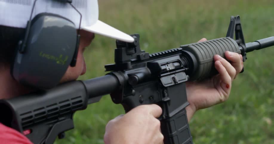 Man shooting a rifle in a wooded area while wearing ear protection