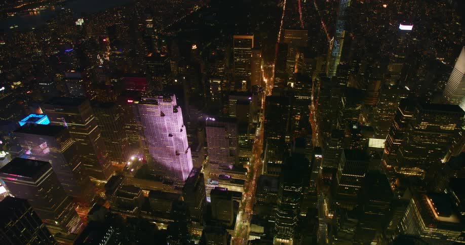 Tall city buildings and street lights illuminate at night
