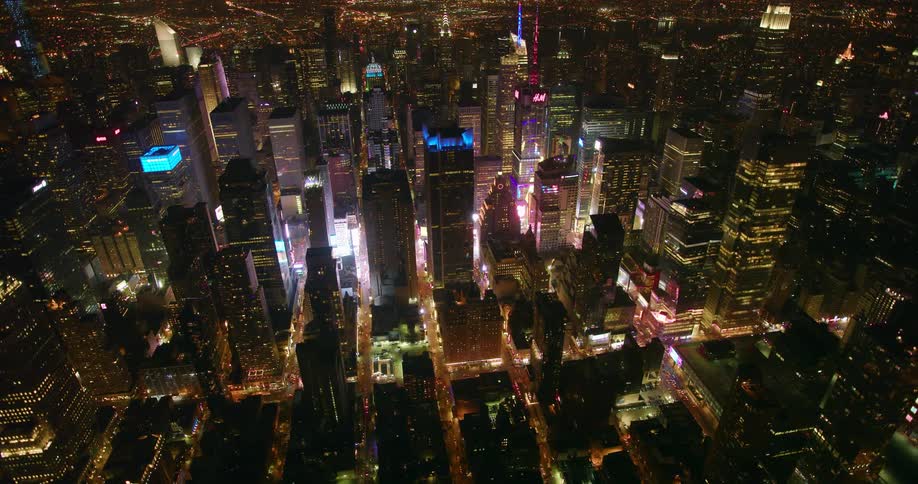 Tall city buildings and street lights illuminate at night