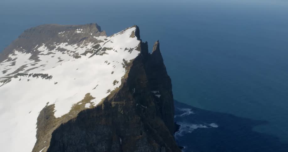 Snow covers the ridge of a cliff on the coast during the day