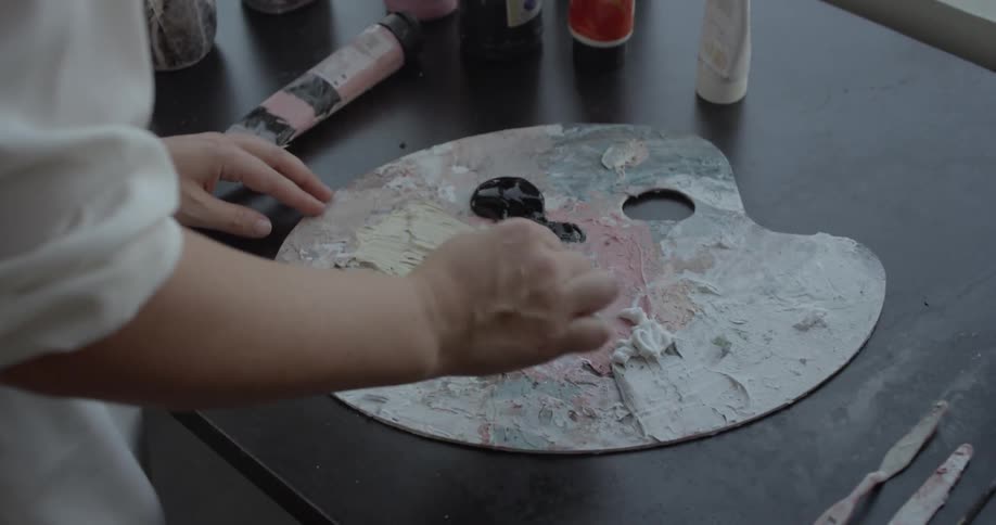 Woman mixing arr paint on a palette lying on a table