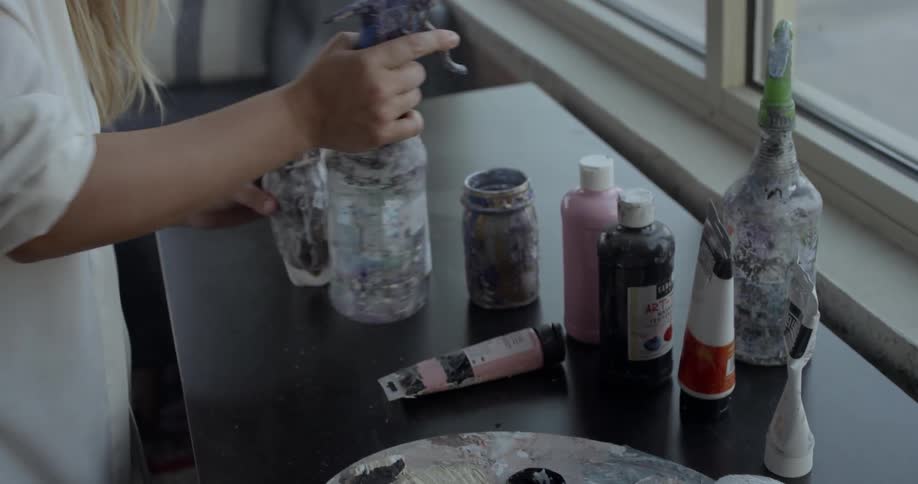 A woman mixes paint in a jar with a brush
