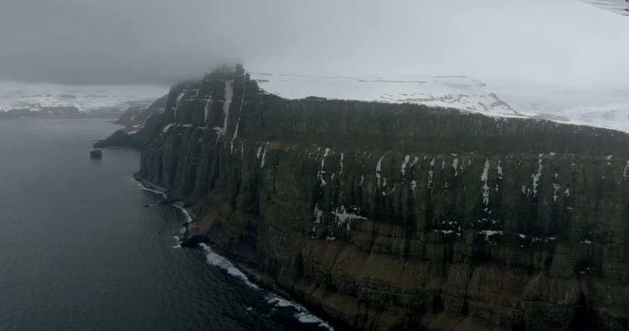 Ocean meets steep bluffs with snowy mountain in background