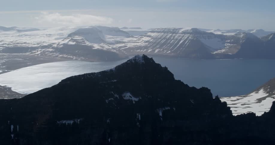 A tall mountain peak looms over a snow-covered coastal view