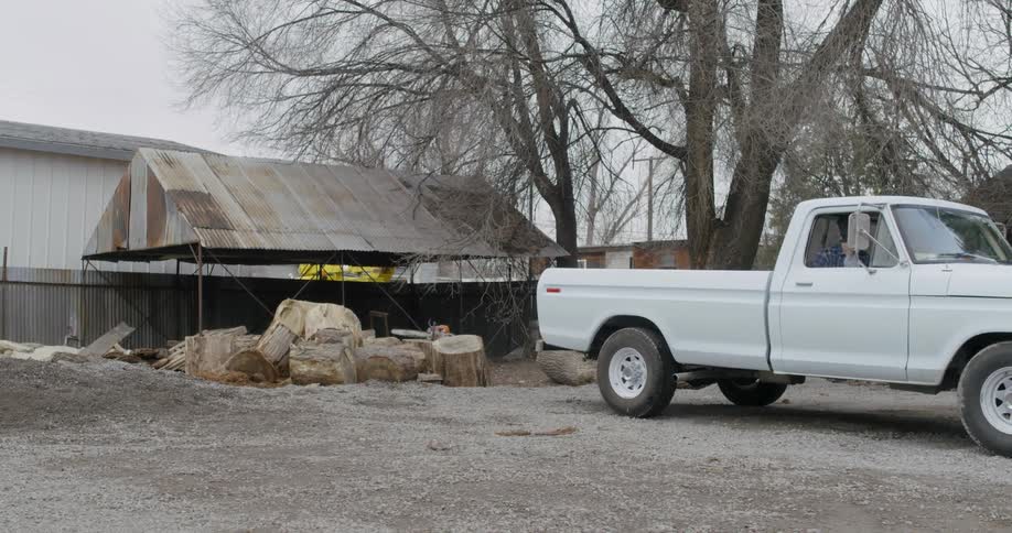 A pickup truck is being backed up to a wood pile in a yard during the day