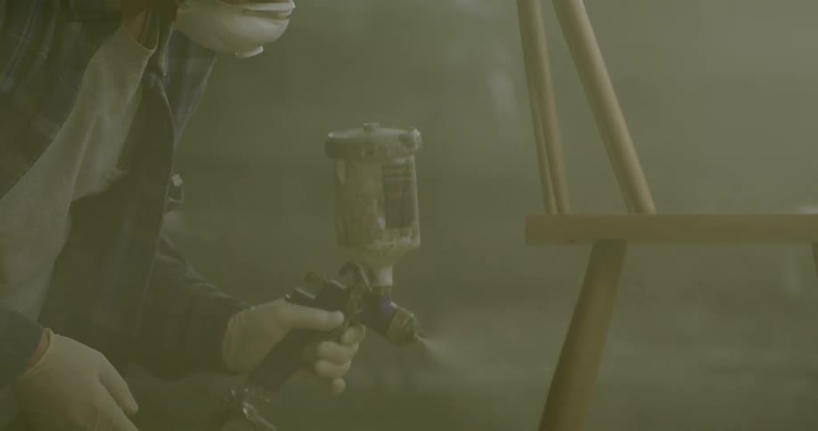A man is spray painting a wooden chair