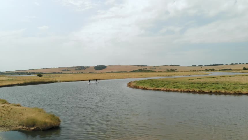 Two people paddle board down a stream