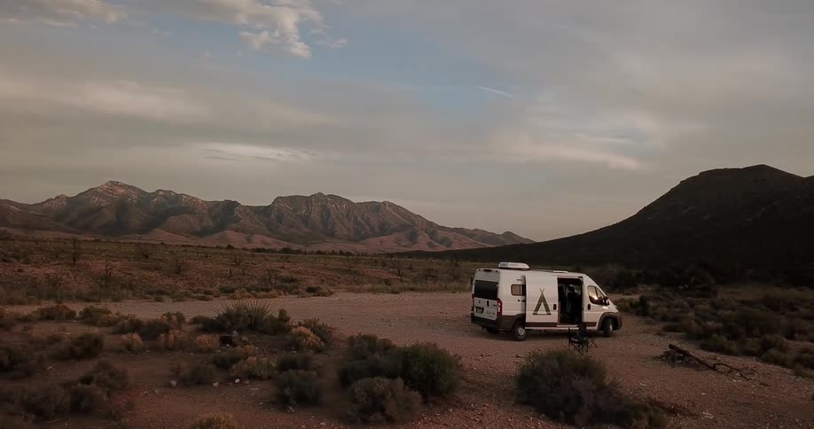 A camper is parked in a desert clearing with the door open and  a chair set up