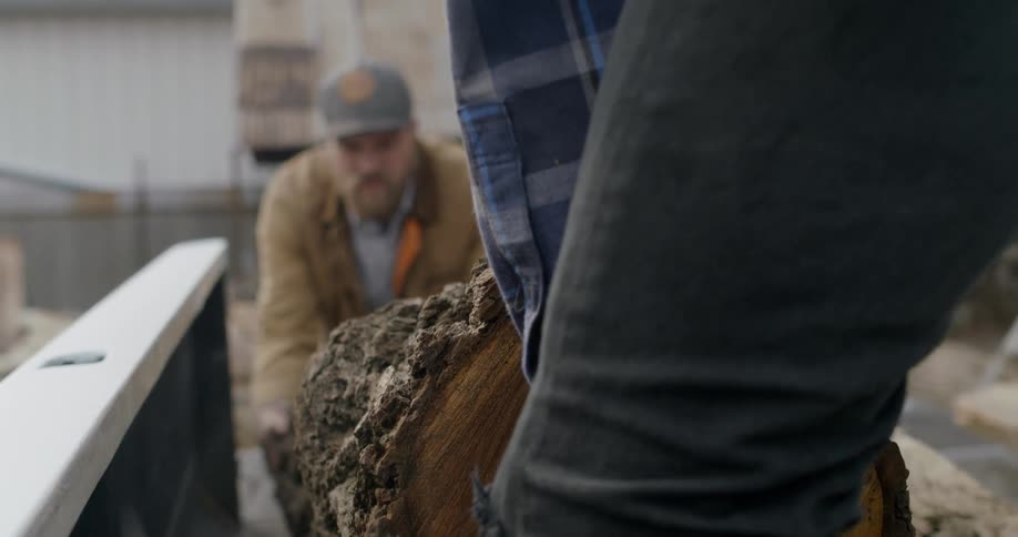 Two men lift a piece of tree trunk out of a pickup truck