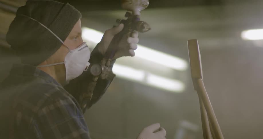 A man sprays paint on a piece of wood