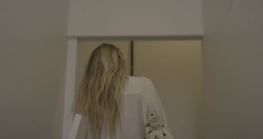 A woman carrying a canvas and bag is walking through a hallway