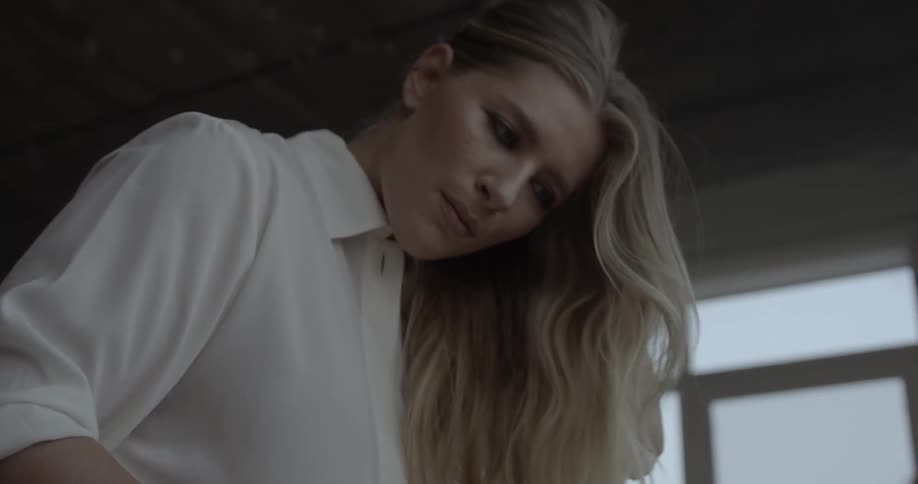 Blond woman looking down and maneuvering something indoors in a city