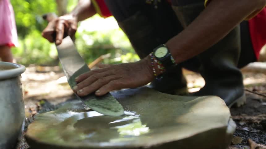 A man sharpening a blade on a wet stone as a little girl walks around in the background