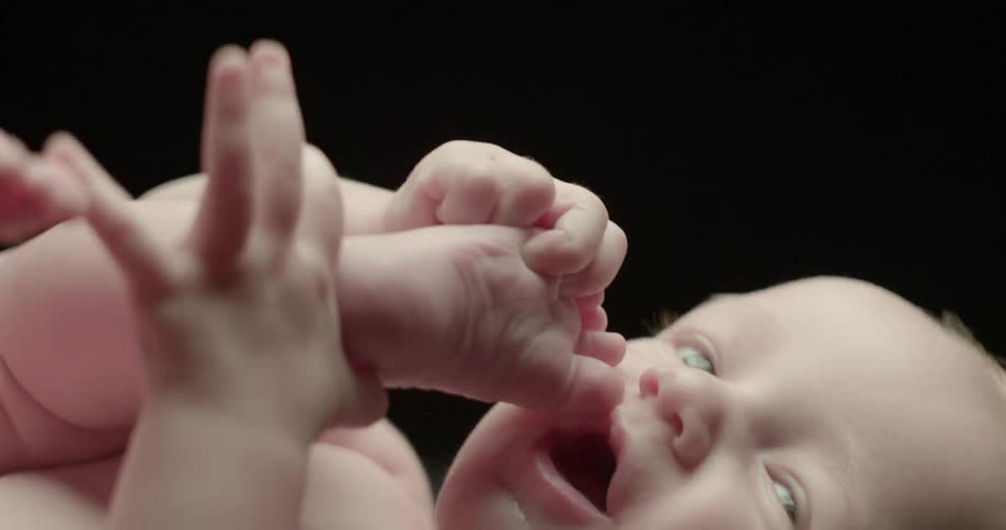 An infant is pulling his feet to his mouth