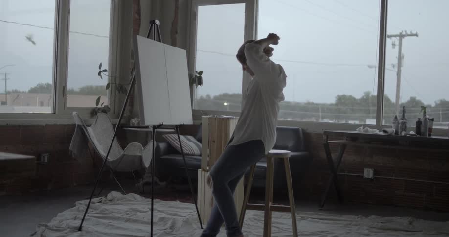 A woman puts her hair up in front of an easel