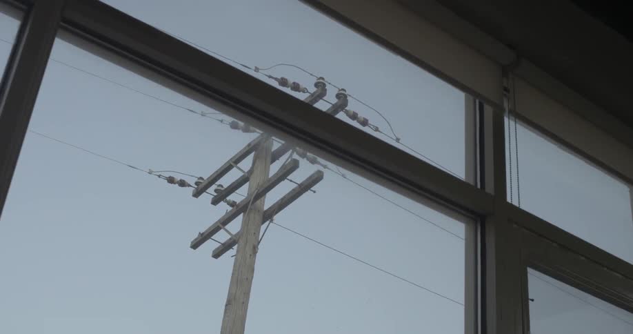 A power pole is being filmed from inside a building through a window