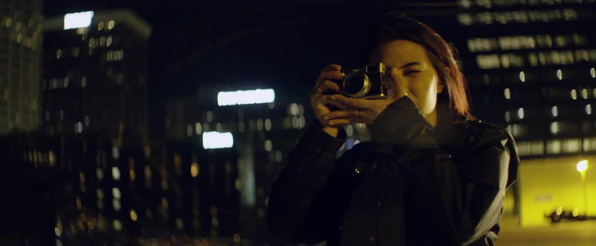 A woman stands outside overlooking a city and takes a photo
