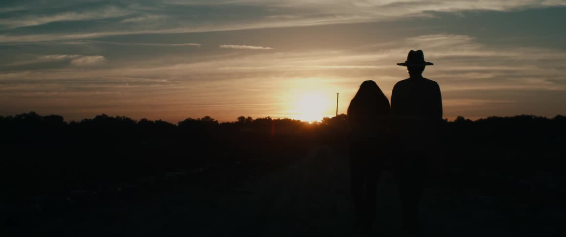 A man and woman walk outdoors at sunset