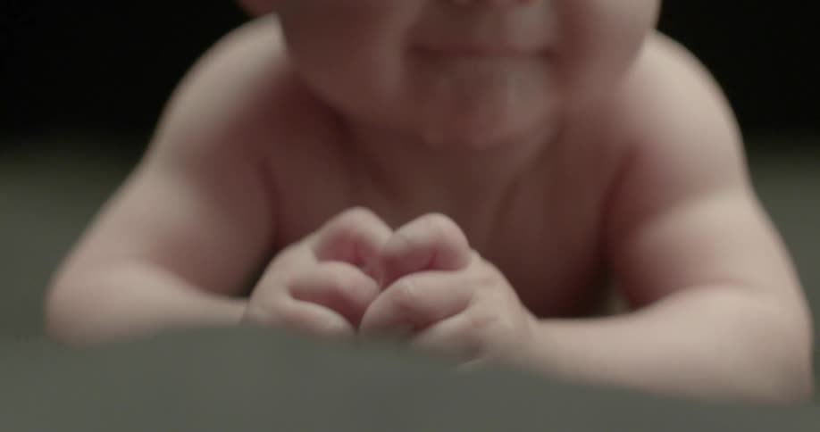An infant drools and smiles while laying on his belly