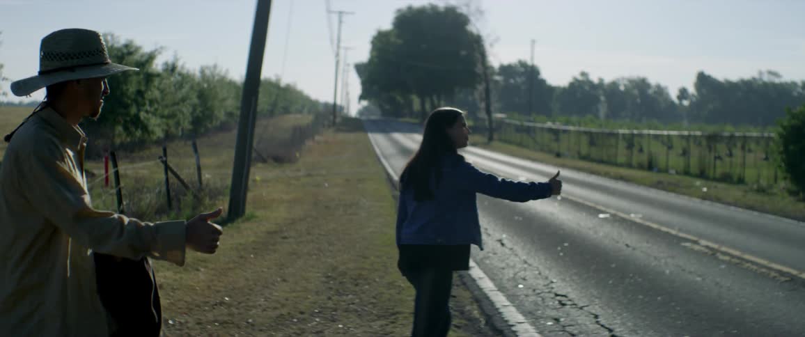 Couple hitchhiking on a paved country road as a vehicle passes them by