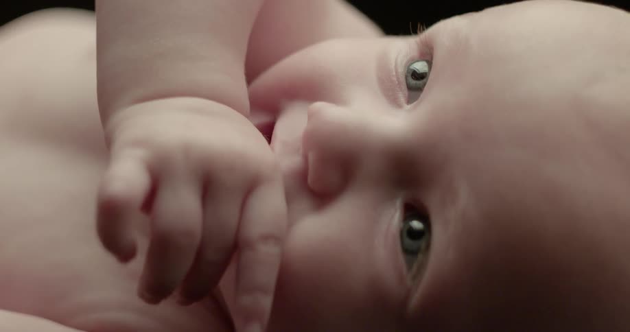 An infant lays and sucks on its fingers