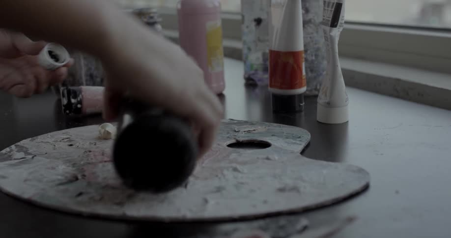 An artist shakes paint and pours it onto a palette