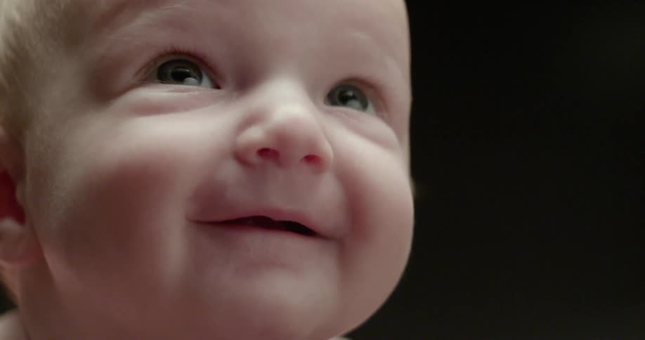 An infant looks up sweetly and smiles with delight