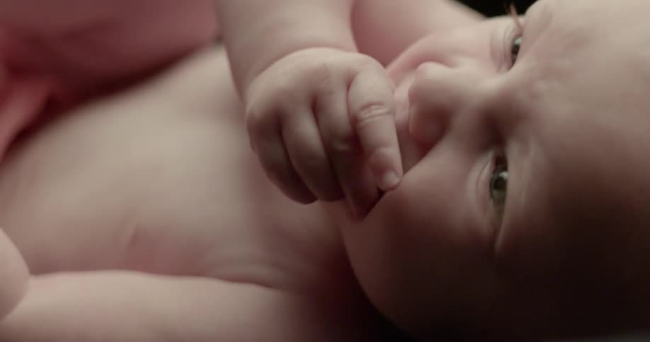 Infant lying on its back and wriggling with its thumb in its mouth