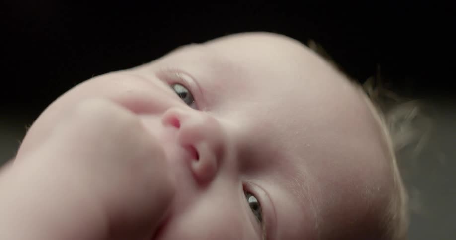 A baby is smiling and chewing on its fist