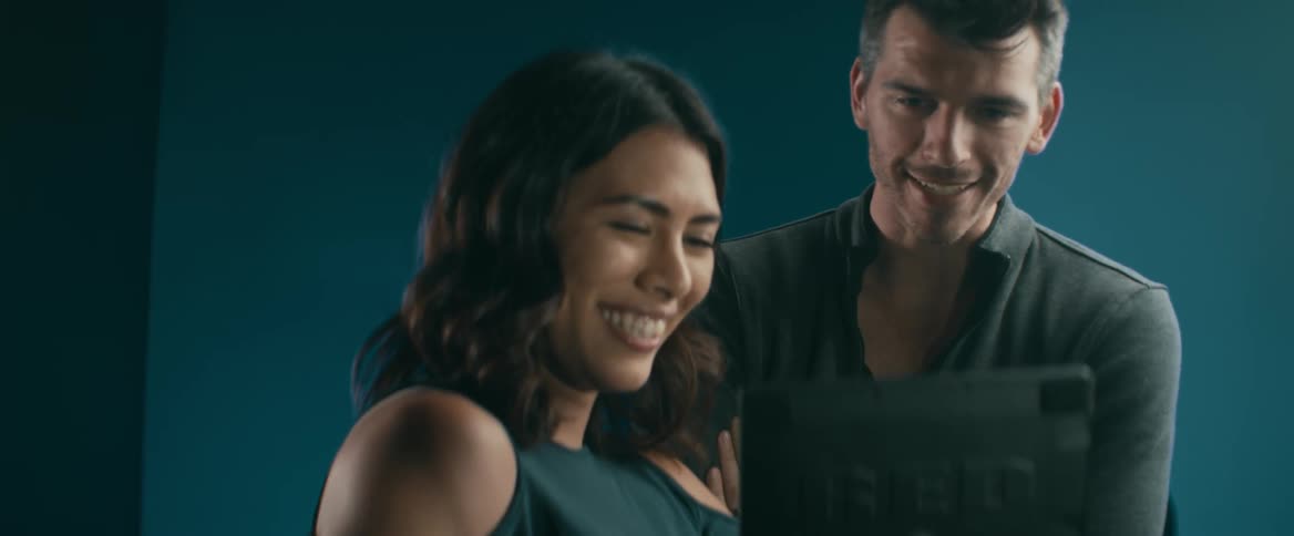 A man and woman are looking at a monitor in a studio and smiling
