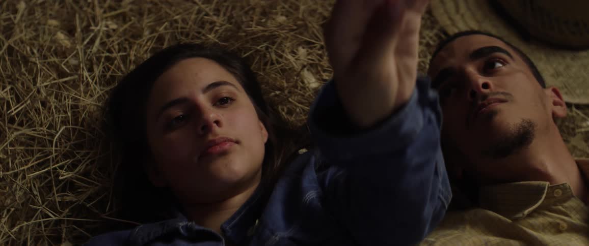 A woman lying in the hay holding her hand up