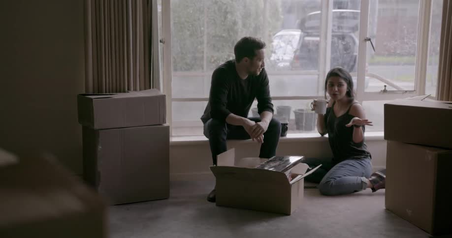 A man and woman sit in an apartment unpacking boxes
