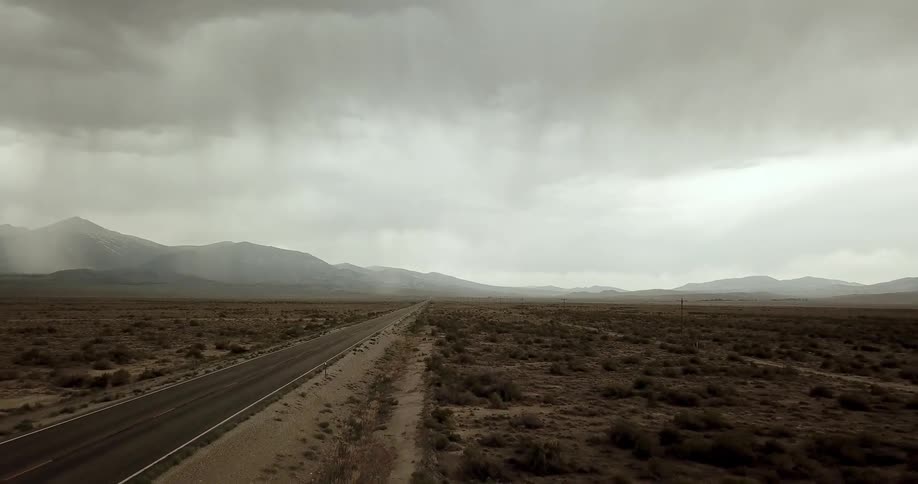 Storm clouds are dropping rain over a desert highway during the day
